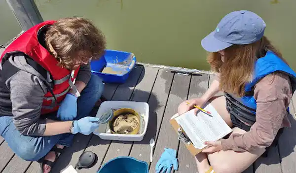 Two students test water samples by a lake