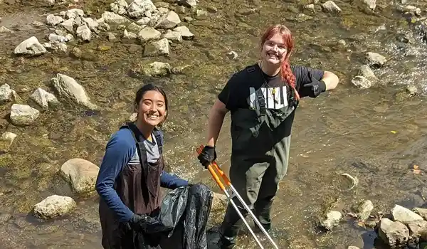 Two students in a creek bed working on a sustainability project