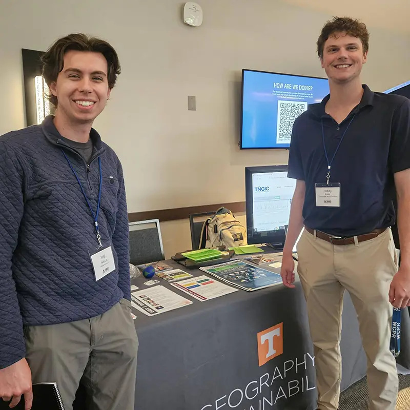Two male students standing in front of a UT table at a conference