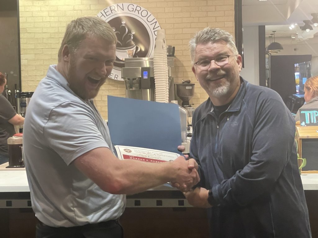 Seth Kannarr shakes hands with another person while receiving his graduate student paper award in a coffee shop.