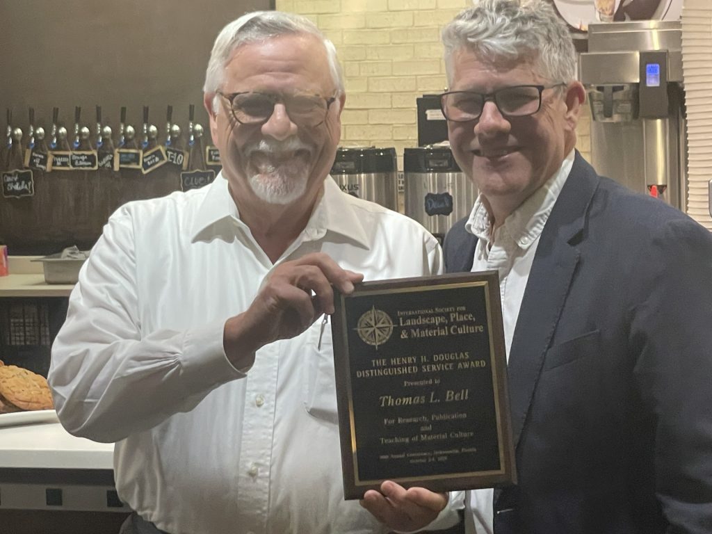 Thomas Bell holds his Distinguished Service Award plaque alongside another person at a coffee shop.