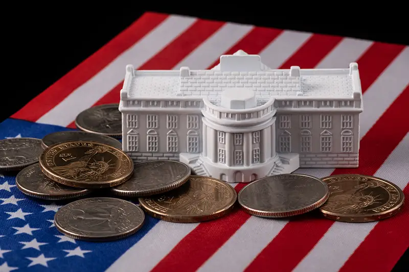 The symbolic residence of the US President, the White House, against the backdrop of the American flag and coins. Image by Max Zolotukhin.